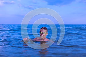 A 10-year-old boy swims in the sea at dawn with glasses for swimming