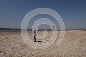 A 10 year old boy in a white sweatshirt and orange vest launches a kite on a deserted beach in solitude