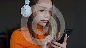 10 year old girl listens to music through headphones and an online smartphone application.