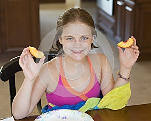 10 year-old girl sitting at a table holding a peach slice in each hand