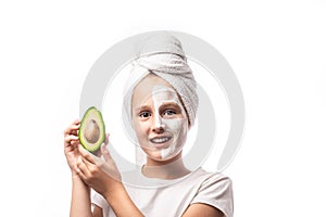 10 years old preteen chilling making clay facial mask and holding avocado fruit. Teenage girl doing anti blemish skin treatment.