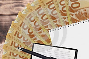 100 Canadian dollars bills fan and notepad with contact book and black pen. Concept of financial planning and business strategy