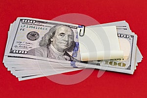 100 dollar bills with black paper clip and sticker paper on red background