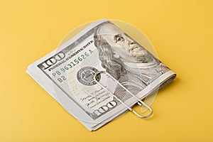The 100 dollar bills are folded in half and held together with a paper clip on yellow background. Closeup view