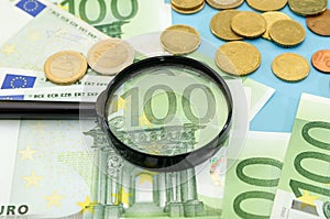 100 euros through a magnifier and coins. Blue background. Financial concept.
