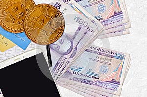 100 Philippine piso bills and golden bitcoins with smartphone and credit cards. Cryptocurrency investment concept. Crypto mining