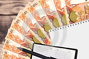 100 Sri Lankan rupees bills fan and notepad with contact book and black pen. Concept of financial planning and business strategy