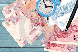 100 Thai Baht bills and alarm clock with pen and envelopes. Tax season concept, payment deadline for credit or loan. Financial