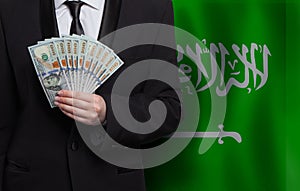 100 US dollar bills money banknotes in hand against flag of Saudi Arabia background