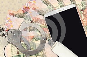 1000 Guyanese dollars bills and smartphone with police handcuffs. Concept of hackers phishing attacks, illegal scam or malware
