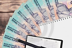 1000 Indonesian rupiah bills fan and notepad with contact book and black pen. Concept of financial planning and business strategy