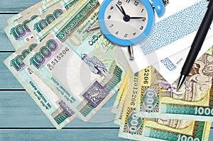 1000 Sri Lankan rupees bills and alarm clock with pen and envelopes. Tax season concept, payment deadline for credit or loan.