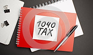 1040 tax sign on sheet of paper on the red notepad with pen