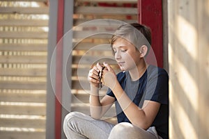 An 11 year old Catholic boy reads the rosary prayer, holds a wooden rosary with 10 beads in his hands.