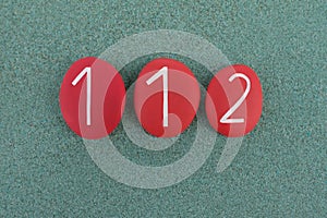 112, Emergency telephone number composed with red colored stones over green sand