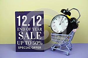 12.12 End of year sale promotion with trolley shopping cart and alarm clcok on yellow background, business background