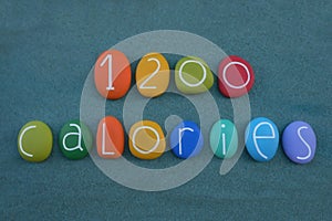 1200 calories diet text composed with multi colored stone letters and numbers over green sand