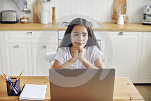 12s girl sit at table in kitchen watching vlog on laptop