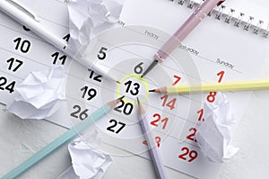13 Friday date as a time deadline. Marked date in the calendar and pencils, pens surround it, paper balls on the office desk