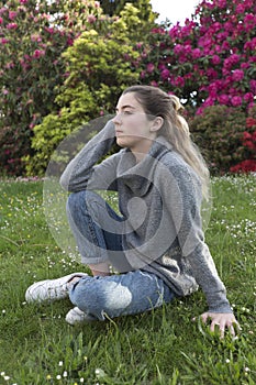 16 year old teenager sitting in a park with grass and flowers.