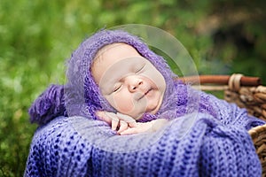 17 day old Smiling newborn baby is sleeping on his stomach in the basket on nature in the garden outdoor.