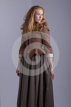18th century woman in brown outfit on plain studio backdrop