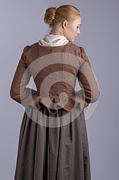 18th century woman in brown outfit on plain studio backdrop