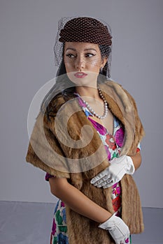 1950`s woman in a colourful dress, hat with a veil and a fur stole against a white backdrop