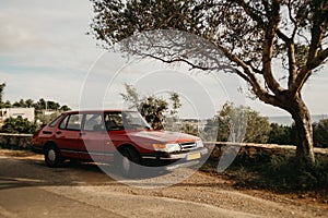 1990s classic red car in dreamy setting on top of a hill with sea view and blue sky