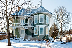 19th Century cottage with painted shingles, protruding half-tower and sheet metal roof seen during a sunny early morning winter