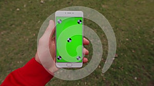 1st person view, blank green screen of smartphone in a male hand walking on a grass