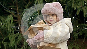 A 2-3 year old girl at the Christmas market holding a small Christmas tree. A child catches the falling snowflakes with