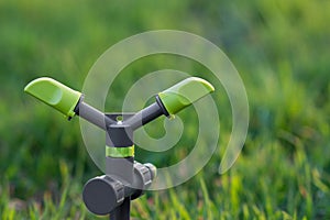 2-arm rotating sprinkler on spike with green grass background