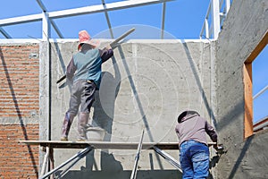 2 Asian builder workers on wooden scaffolding are plastering and polishing concrete wall room in house construction site