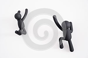 2 black 3D puppets climbing over a white background, human character , person hanging from a white wall, one trying to help the
