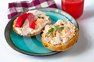 2 canapÃ©s with salmon spread and fresh cheese on blue plate, glass of juice, cloth