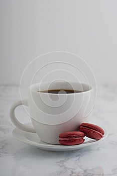2 chocolate french macarons with a cup of coffee on a white marble table.