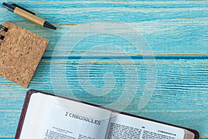 2 Chronicles open Holy Bible Book, notebook, and pen on a rustic wooden background with copy space