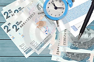 2 Colombian pesos bills and alarm clock with pen and envelopes. Tax season concept, payment deadline for credit or loan. Financial