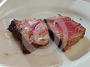 2 delicious and juicy pieces of medium steak served on a white plate.