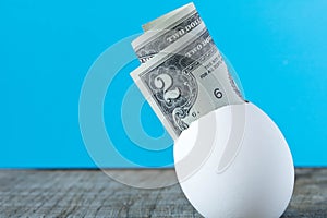 2 dollar bill in an egg shell. On a turquoise background. The co