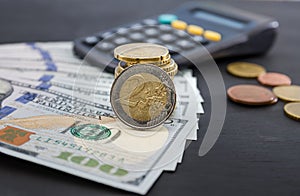 2 euro coin in a hand against the background of dollars and a calculator. Business concept. Black background.