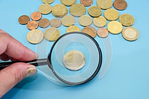 2 euro coin through a magnifying glass. Blue background. Financial concept. Lots of coins. Savings concept.