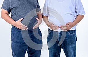 2 fat man are standing and using their hands to hold their belly fat