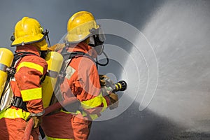 2 firefighters spraying water in fire fighting with dark smoke b