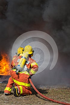 2 firemen spraying water in fire fighting with fire and dark smoke background