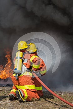 2 firemen spraying water in fire fighting with fire and dark smoke background