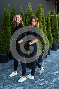 2 girls in black tracksuits posing near thuja.