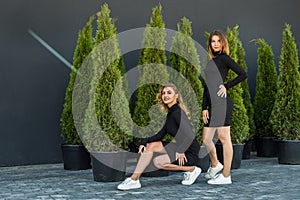 2 girls in black tracksuits posing near thuja.