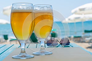 2 glasses filled with ice-cold beer standing on a table at the beach